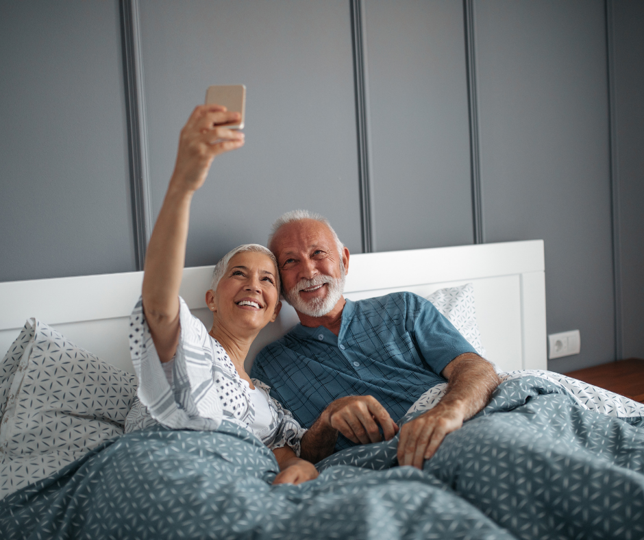 An older man and woman in bed taking a selfie